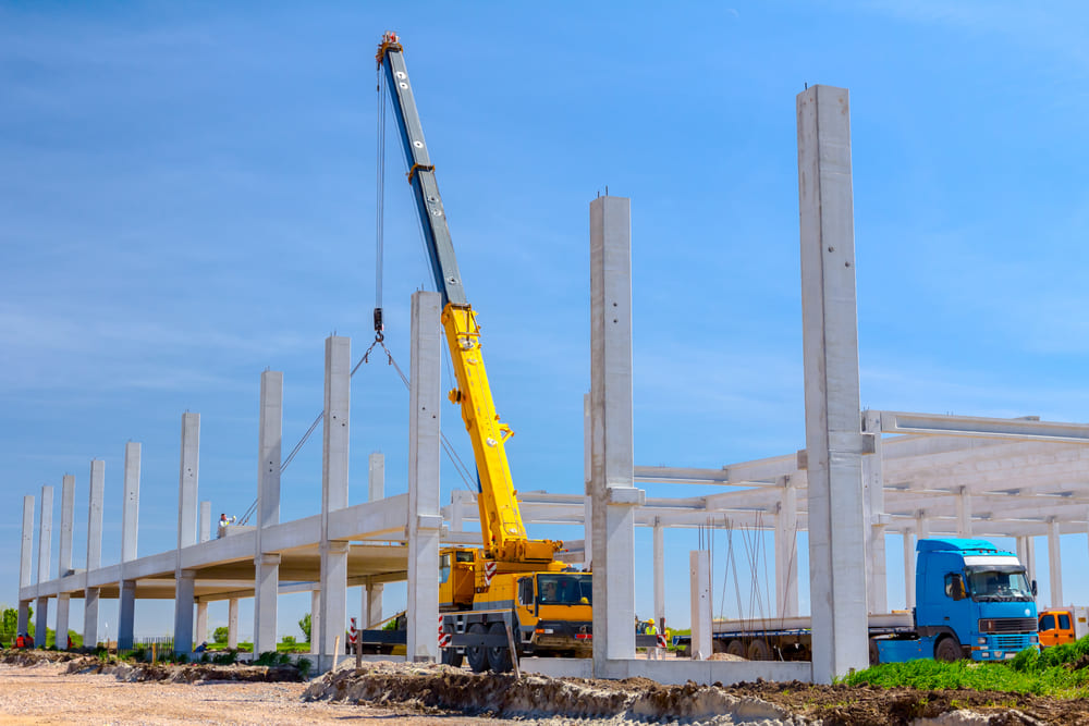 Grue en train de lever une poutre béton pour
poursuivre la construction d’un bâtiment industriel